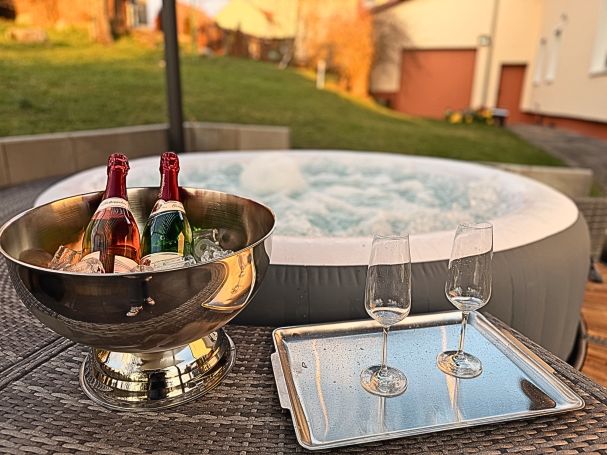 Outdoor-Whirlpool im Ferienhaus Taufstein mit gekühltem Sekt und zwei Gläsern im Garten zur blauen Stunde